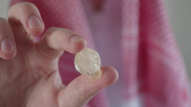 A man in Arab traditional clothing with a headscarf, wearing a Gulf Arab dress, holding a citrine natural stone in his hand