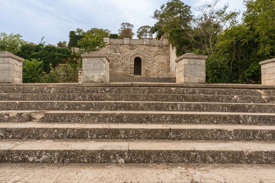 Historic stone Mithridates Staircase leads to top of Mount Mithridates. Ancient arched doorway, surrounded by weathered walls and lush greenery, evoking sense of timelessness and mystery