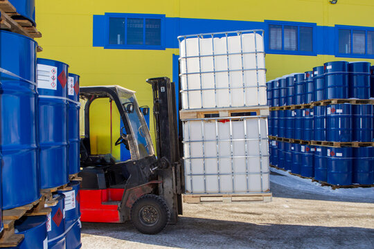 Plastic barrels are transported on forklift. Territories of chemical products warehouse. Forklift with IBC on pallets. Unloading petroleum near warehouse. Forklift near industrial building