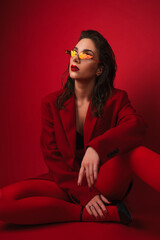 Young Woman In Red Suit With Red Lips And Sunglasses Posing On The Red Background