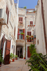 Narrow stone alley in Polignano a Mare featuring traditional whitewashed houses decorated with colorful potted plants, embodying southern Italian coastal charm
