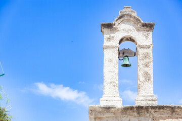 White bell tower standing near green bell, overlooking azure skyline of Polignano a Mare, Puglia,...