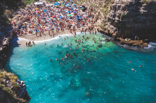 Aerial view capturing swimmers and sunbathers on Lama Monachile beach, Polignano a Mare, Puglia, under bright summer sunlight