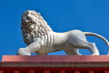 A majestic white lion statue atop a historic building conveys authority with its detailed mane and powerful stance. One paw rest on a sphere, symbolizing guardianship and cultural significance.