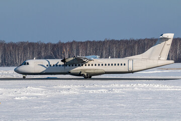 Fototapeta premium White passenger turboprop aircraft taxiing on the main taxiway at a winter airport