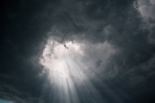 Rays of light through the hole in the dark stormy clouds in the sky.