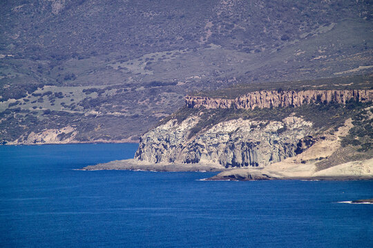 the dramatic trachyte and ignimbrite cliffs along the coast of Bosa Marina in Sardinia, Italy. The featured rocky coastline includes areas known as Cane Malu, popular for its natural pools and diving 
