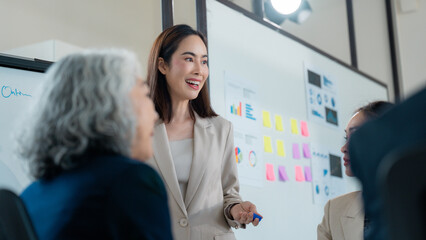 Businesswoman leading a meeting with colleagues, using a whiteboard and sticky notes to present data and discuss strategies