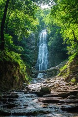 Naklejka premium Waterfall in green forest. Water stream flows over rocks. Sunny light shines through trees. Nature landscape view. Natural environment background.