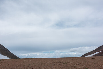 Minimalist layered landscape with high alpine pass and low cloudy sky in changeable weather....
