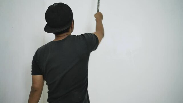 Asian man repairman painting walls of apartment in white using paint roller, 4k video. House finishing services concept.