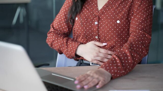 Close up. Young female hands holding massaging stomach. Businesswoman feels stomach pain sitting at workplace in business office. Sick woman suffers from gastritis, menstruation, poisoning or bloating