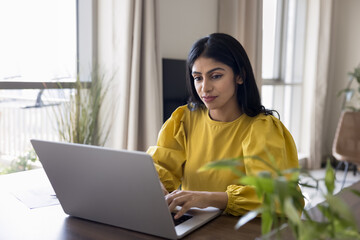 Young Indian woman browsing and purchasing services, or studying online, watching tutorials,...