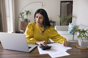 Young Indian woman sit at table with papers and laptop, controlling personal incomes and monthly...