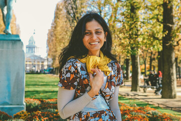An Indian model wearing a floral dress and an ochre yellow scarf is smiling as she poses in a...
