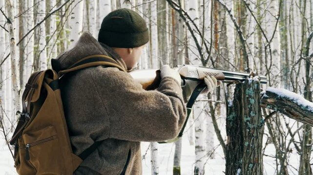 A hunter with a gun in the winter forest takes aim and prepares to shoot. Tracking and hunting wild forest animals.