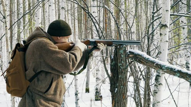 A hunter in a winter forest takes aim and shoots a wild animal with a gun. Tracking and hunting wild forest animals. Hunting is a way of life.