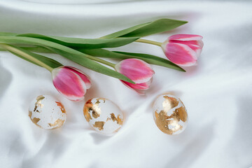 Painted in gold Easter eggs on a white silky background with tulips. Easter  backgorund.
