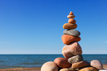 Rock zen pyramid of white and pink pebbles on a background of blue sky and sea.