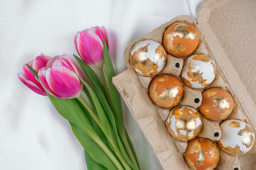 Painted in gold Easter eggs in a carton  on a white silky background with tulips. Easter  backgorund.