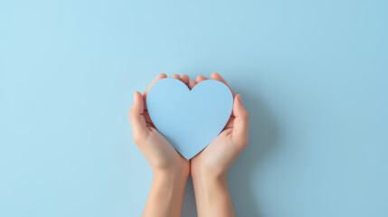 Fototapeta premium Two hands holding blue heart on light blue background, symbolizing love and care