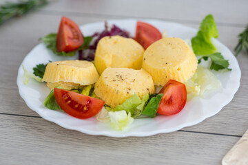 Small steamed omelette with tomatoes and greens on a wooden table
