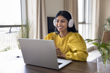 Young Indian woman wearing headphones listening audio course to improve foreign language knowledge,...