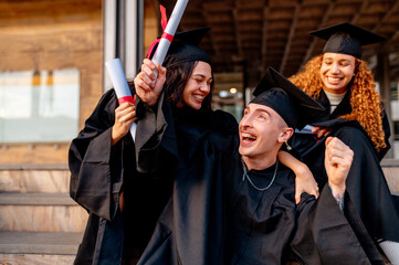 Multiracial graduates wearing gowns and mortarboards are holding diplomas and celebrating...