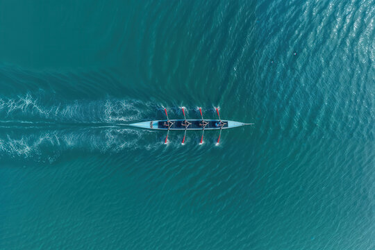 Aerial view of a rowing team in synchronization moving across turquoise water creating ripples and reflections