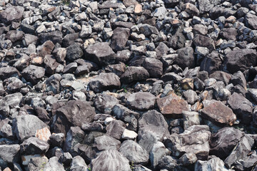 assortment of rocks and stones in varying shapes and sizes. The rocks, predominantly in shades of dark gray, black, and brown, are compacted together, creating a rugged and irregular texture.