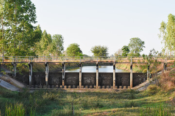 small dam or water control structure with a bridge on top. The dam appears to be constructed of concrete and features vertical supports, providing strength and stability.
