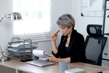 Elder business woman is reading  reviewing and writing reports