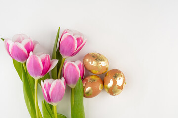 Golden brown eggs with tulips on a white background, top view. Easter festive banner.