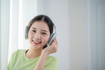 Naklejka premium Young woman enjoys music while wearing headphones and smiling in a bright, airy room during daytime
