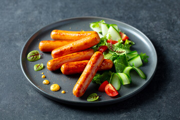 Roast sausages with vegetable salad on a plate. Dark background. Close up.