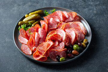Cured meat, sausage assortment platter, antipasti, charcuterie with olives and pickles. Dark background. Close up.