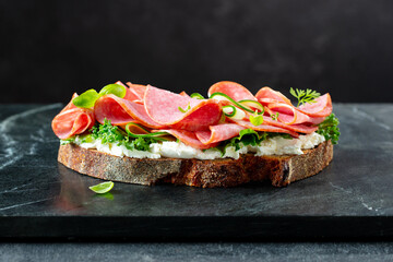 Salami sandwich with cream cheese, green salad and fresh micro greens on a marble board. Dark background. Close up.