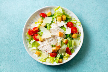 Caesar salad with chicken on a white plate. Blue background. Close up. Top view.