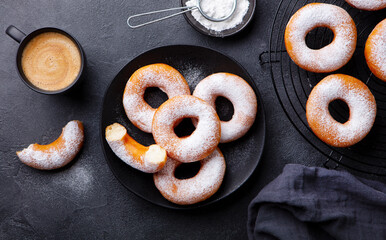 Donuts with sugar powder on black plate with cup of coffee. Dark background. Top view.