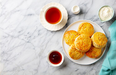 Scones, tea cakes with jam, clotted cream with tea. Traditional British teatime. Marble background. Copy space. Top vie