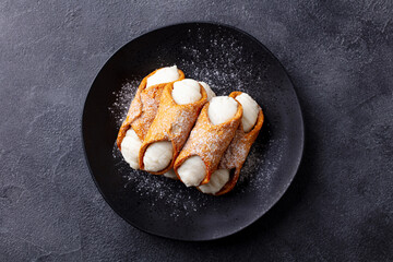 Cannoli Italian pastry on a black plate. Grey background. Close up. Top view.