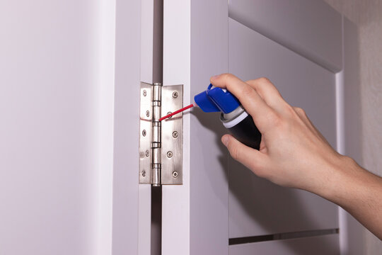 Close up of man hand spraying lubricant on door hinge to prevent door squeaking and rust