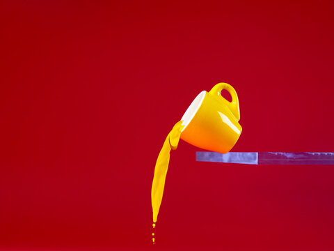 Close-up of a yellow mug on a shelf tipping over with yellow liquid pouring out