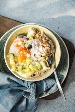 Overhead view of a bowl of yogurt with granola, kiwi fruit, tangerines, grapes and honey
