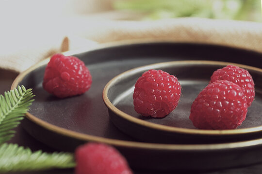 Close-up of a plate of fresh raspberries on a table with foliage