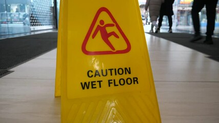 Yellow sign with the inscription caution wet floor standing on a wet floor in a shopping mall. People passing by the sign with the inscription about wet floor. Cleaning.