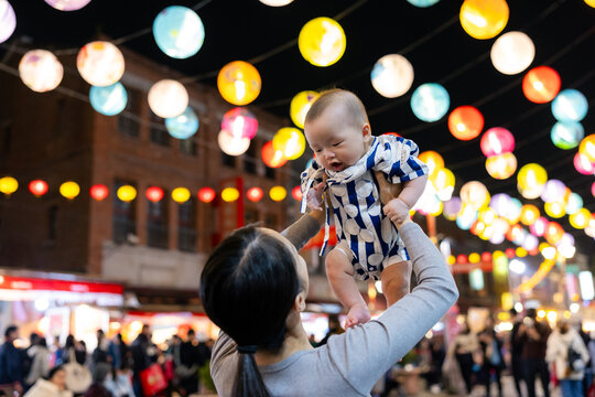 Mother lifting baby under colorful lantern lights