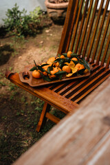Tangerines on a wooden garden chair. Citrus harvest in the garden side view. Ripe tangerines are collected on a tray
