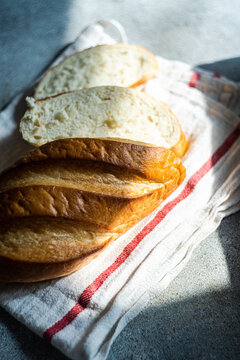 Close-up overhead view of a loaf of freshly sliced homemade white bread on a tea towel in sunlight