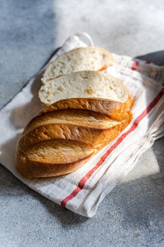 Close-up overhead view of a loaf of freshly sliced homemade white bread on a tea towel in sunlight